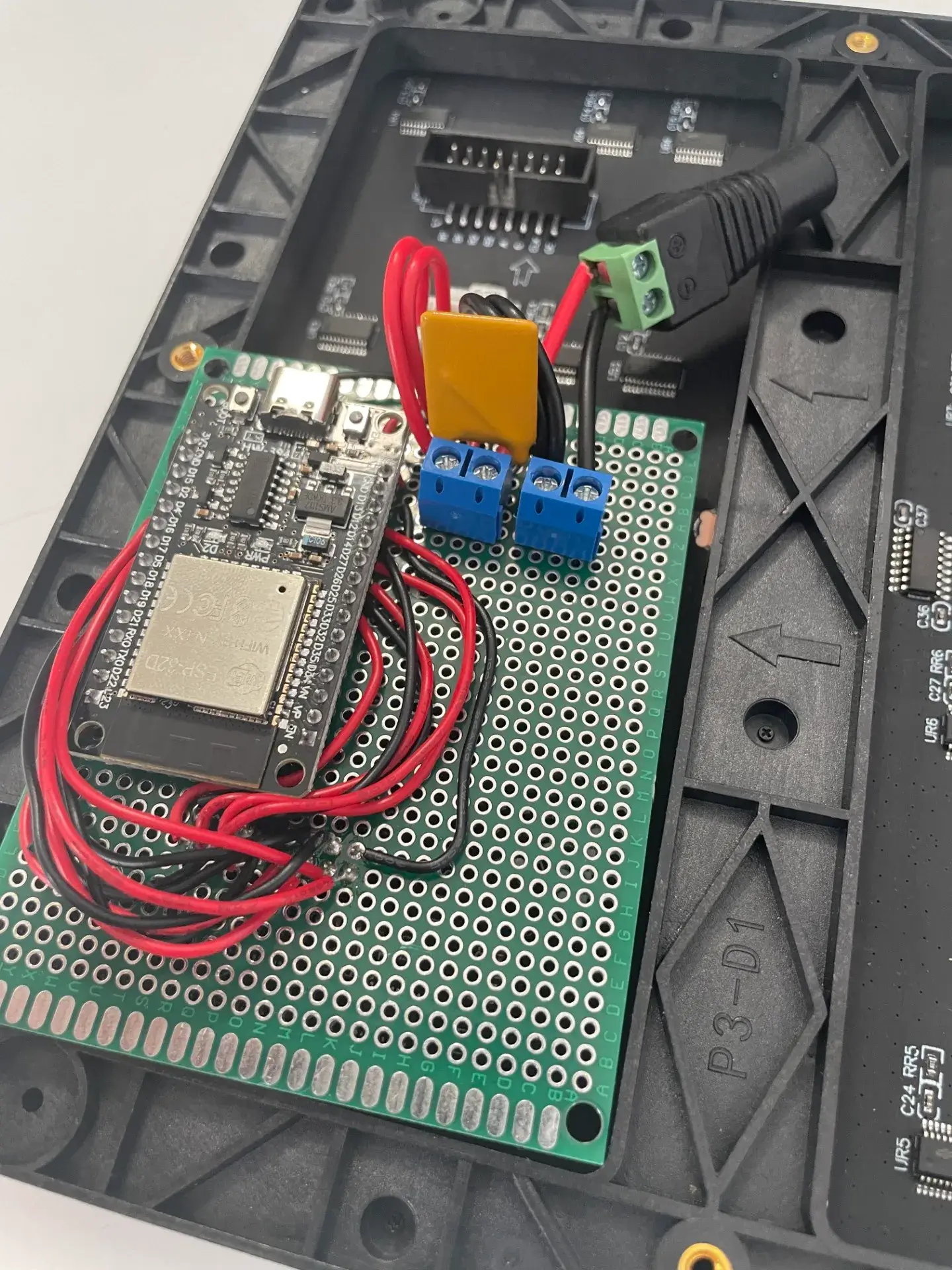 Lochrasterplatine aus der Nähe: ESP32 mit roten und schwarzen Drähten, zwei blaue Schraubklemmen und die Buchse für das Netzteil