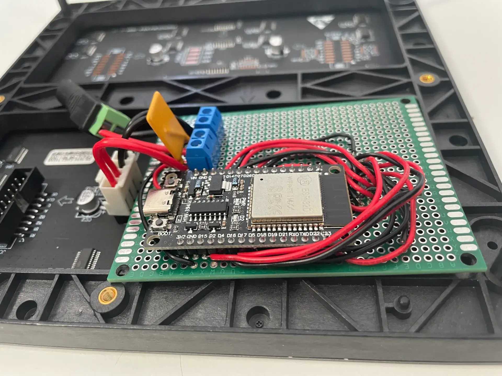 ESP32 auf der Lochrasterplatine von der Seite: USB-C-Buchse vorn, dahinter die blauen Schraubklemmen und das Stromkabel zur Matrix