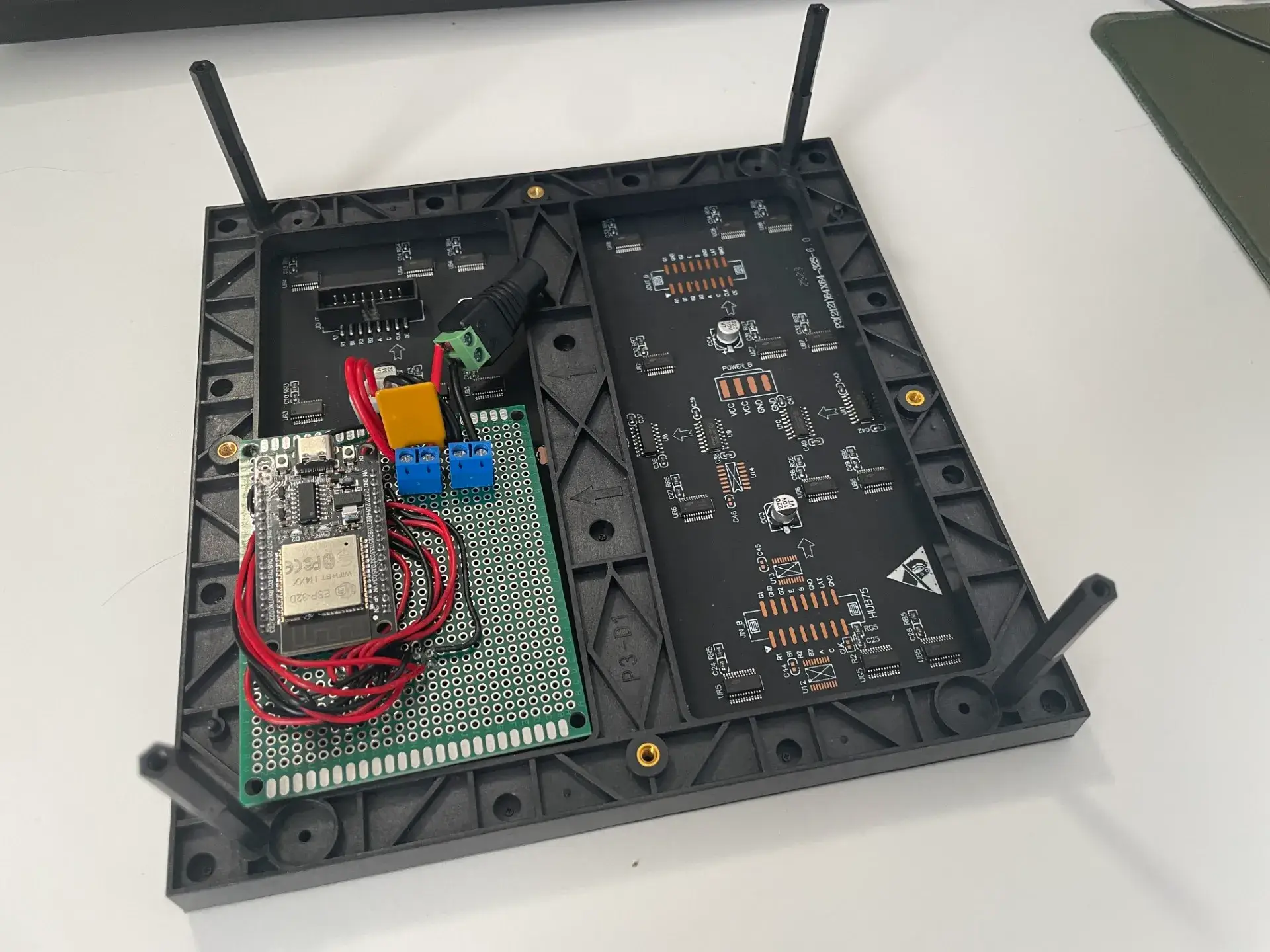 Rückseite der LED-Matrix schräg von oben: links die grüne Lochrasterplatine mit dem ESP32, an den Ecken vier schwarze Abstandshalter