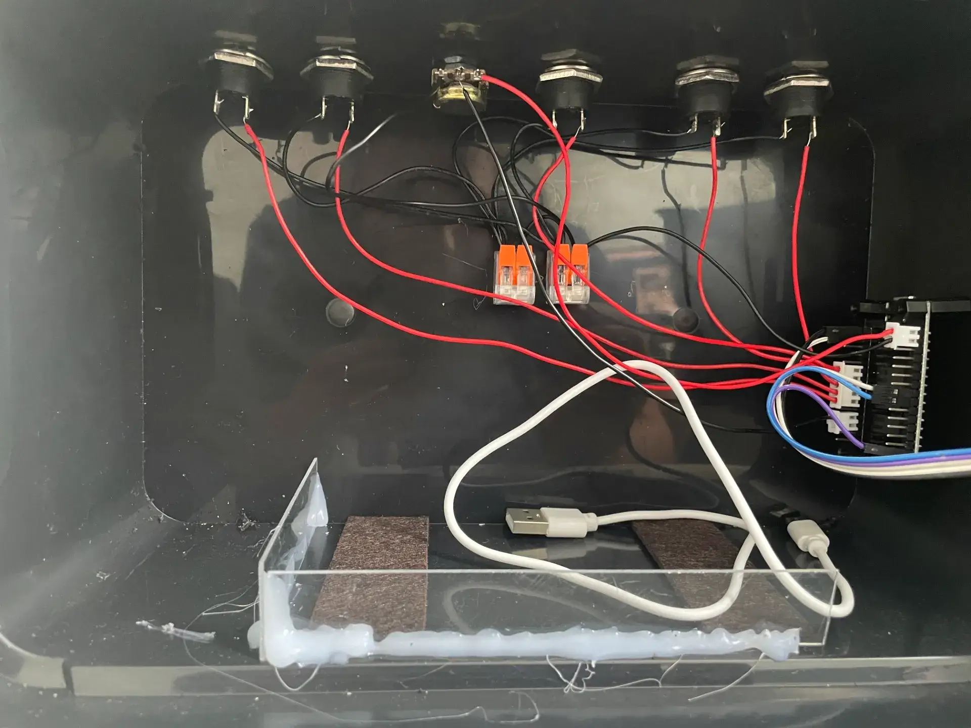 Blick in die Box: rote und schwarze Drähte von den Tastern zum ESP32, zwei Schnellsteckklemmen und ein Fach aus Plexiglas mit USB-Kabel für die Powerbank