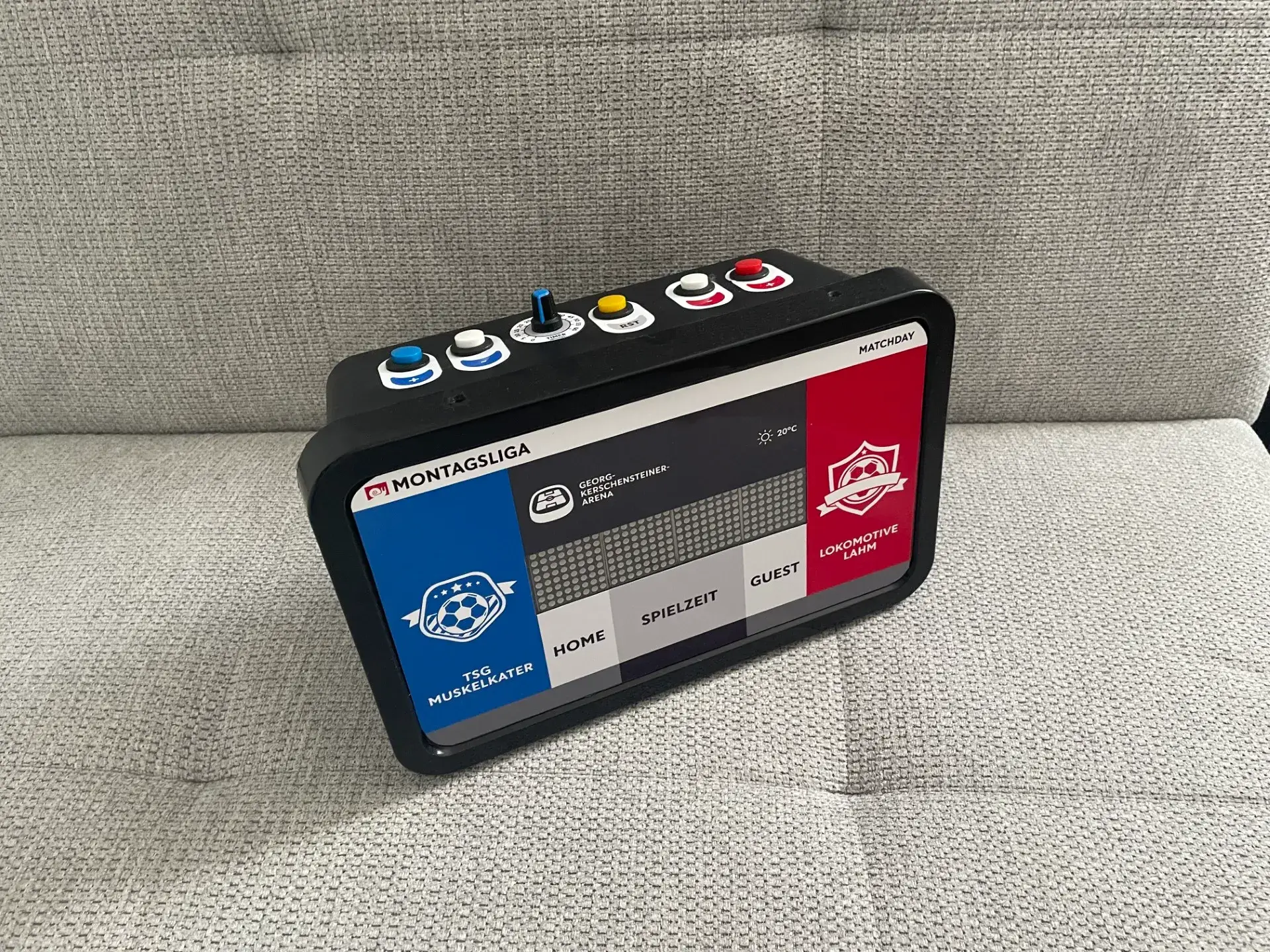 Die fertige Punktestandsanzeige auf einem Sofa: schwarze Box mit blauem Feld für TSG Muskelkater, rotem Feld für Lokomotive Lahm und der LED-Matrix dazwischen